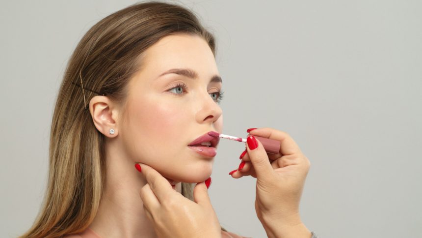 Makeup artist or stylist applies lipstick to the lips of the female model. Applying lipstick.