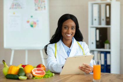 Positive black nutritionist with clipboard creating healthy meal plan for patient at clinic, blank